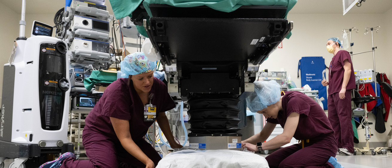 Two nurses put Droste Drape on base of OR bed.