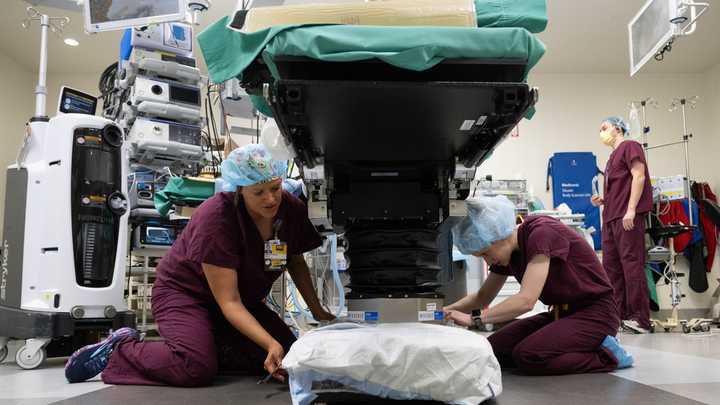 Two nurses put Droste Drape on base of OR bed.
